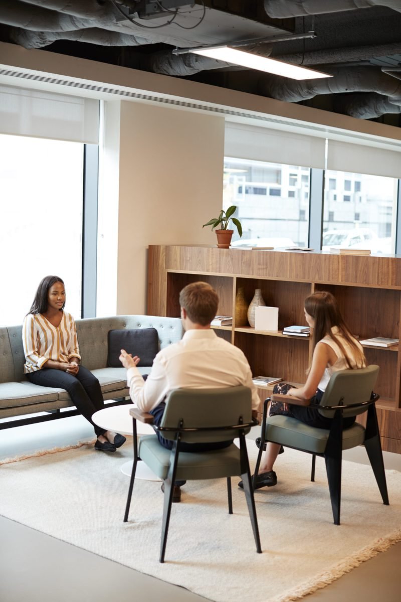 Businessman And Businesswoman Interviewing Female Candidate In Office At Graduate Recruitment Assessment Day