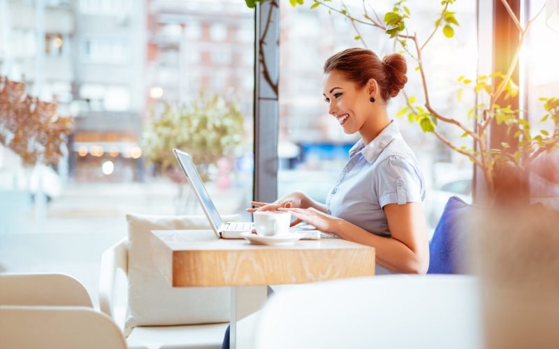 Young smiling businesswoman on a break in a cafe. She is working at laptop.
